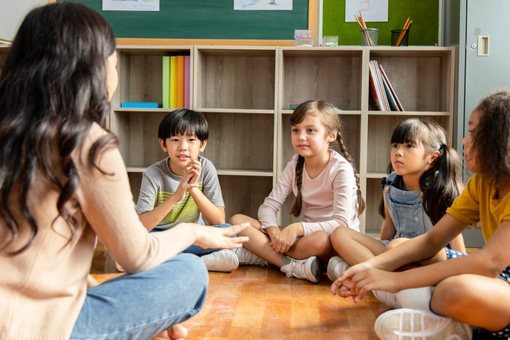niños con una maestra sentados en el suelo haciendo educación respetuosa