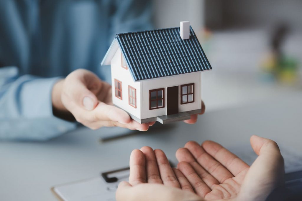 manos manos sosteniendo una maqueta de una casa de seguro de hogara para explicar qué seguros se puden desgravar en la renta