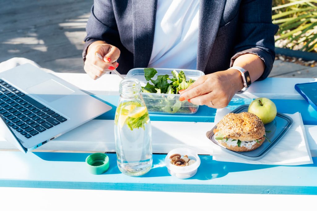 una persona teniendo una alimentación saludable en el trabajo, mientras come al aire libre comida sana y el portatil al lado