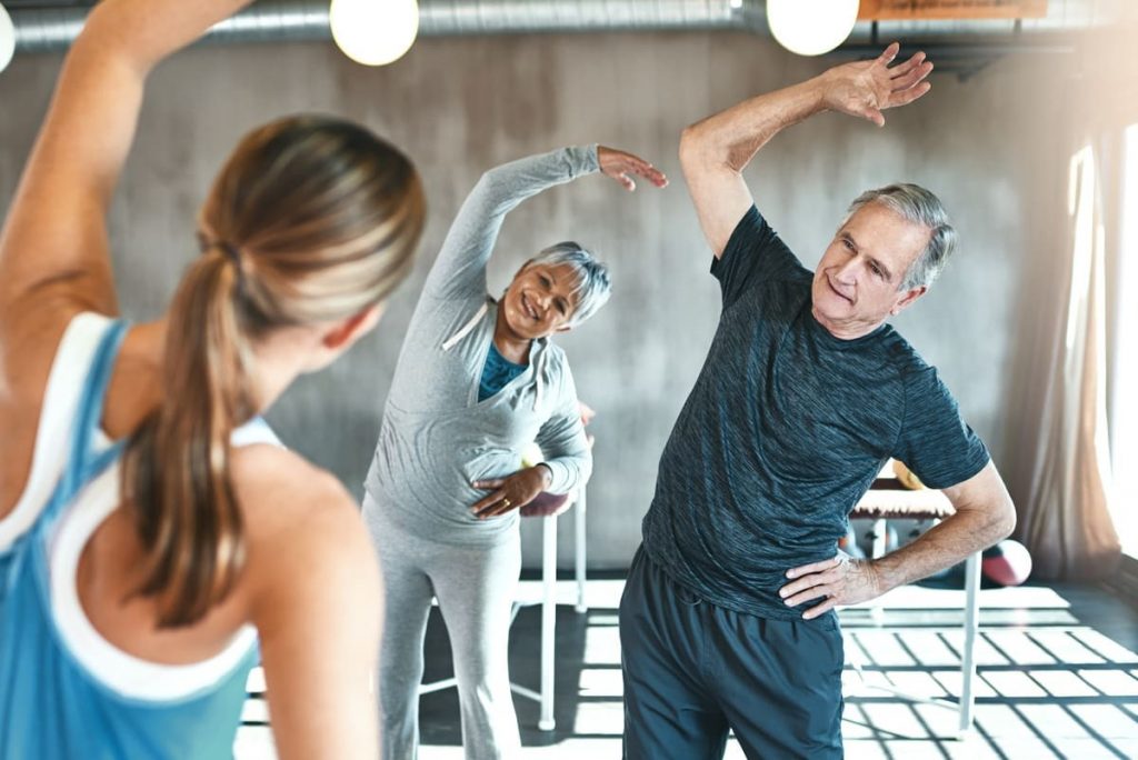 un hombre y una mujer con una entrenadora haciendo ejercicios de pilates para mayores